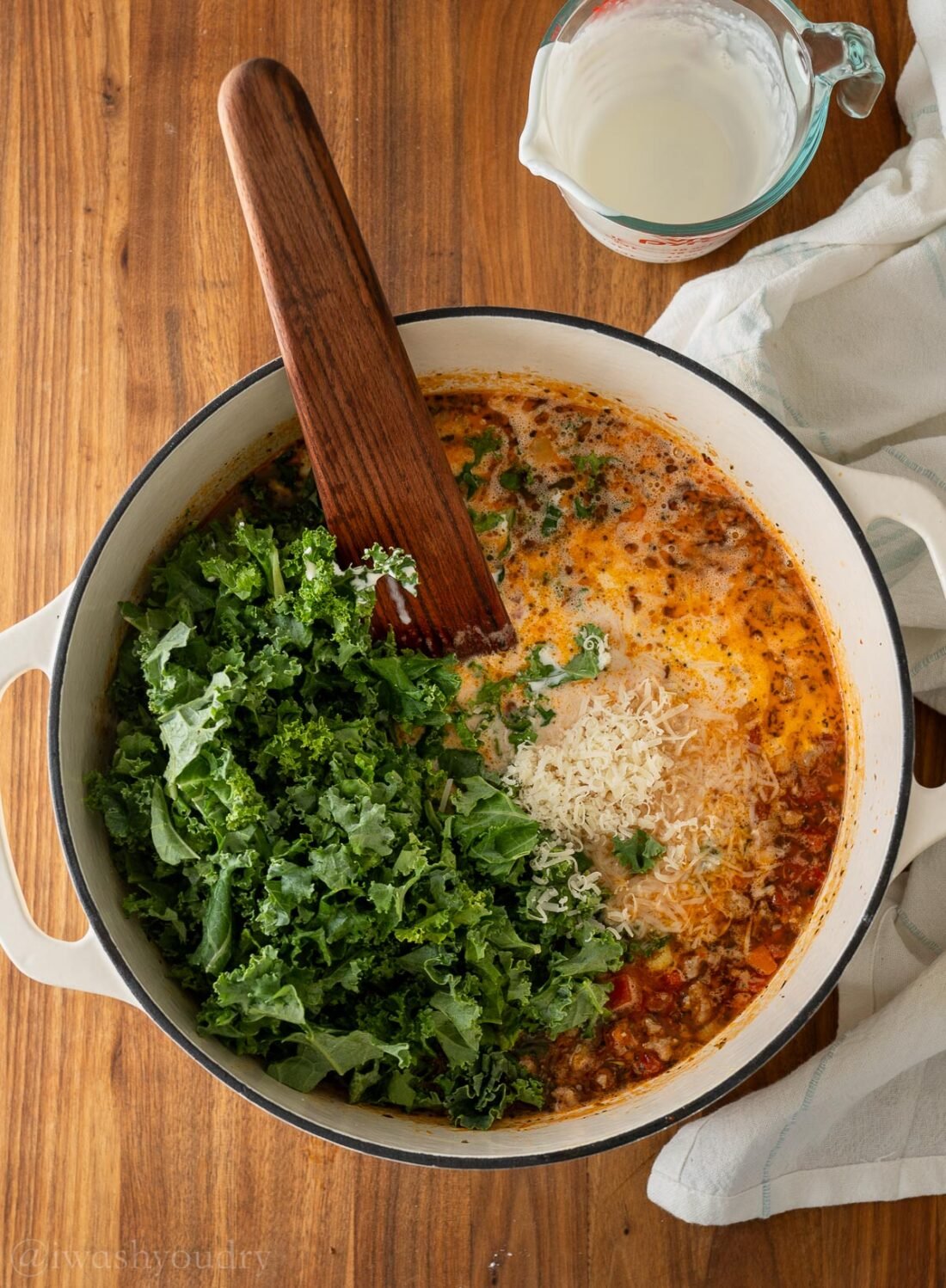 Kale and parmesan cheese in pot of soup with wooden spoon.