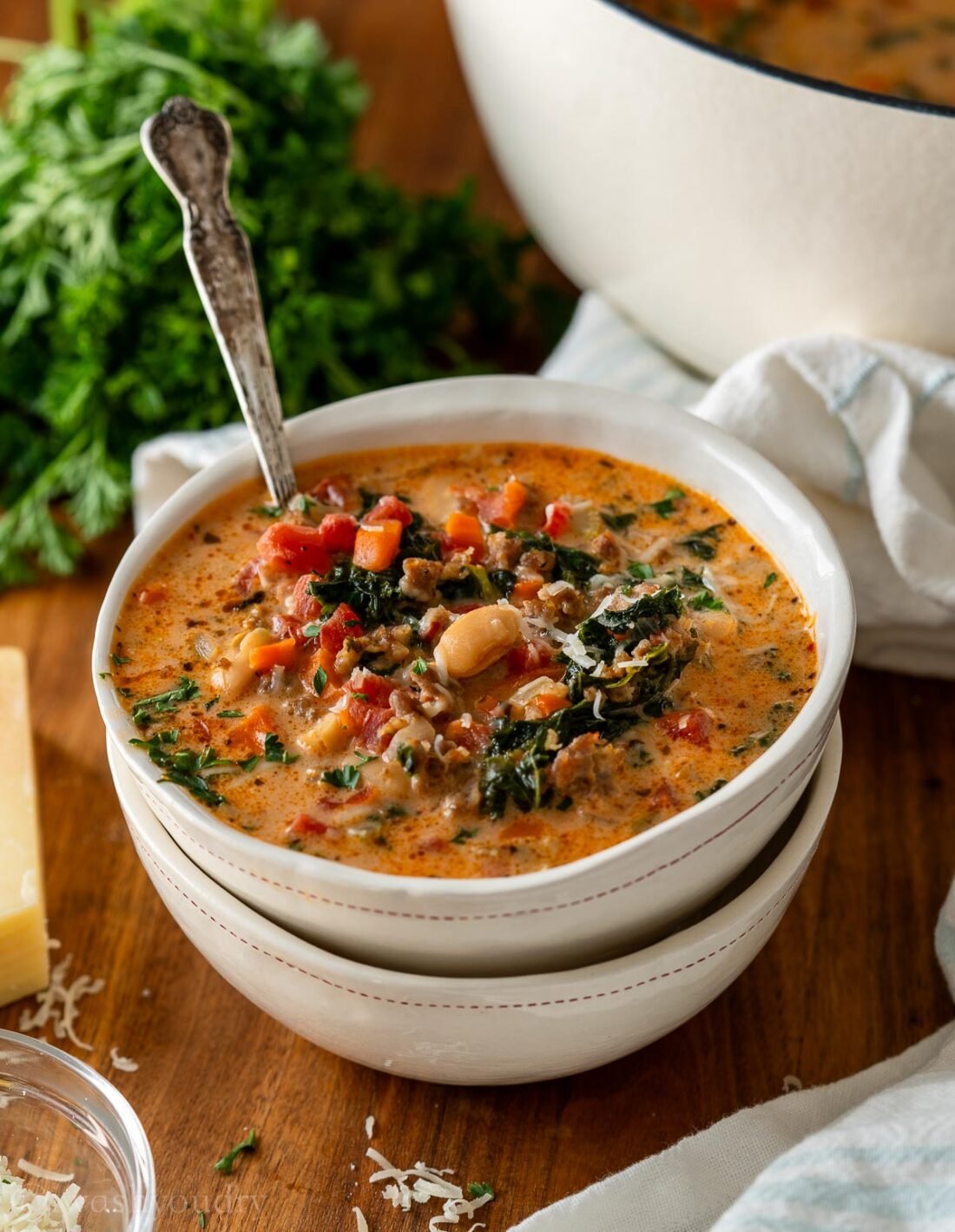 hearty italian soup in white bowl with spoon inside.