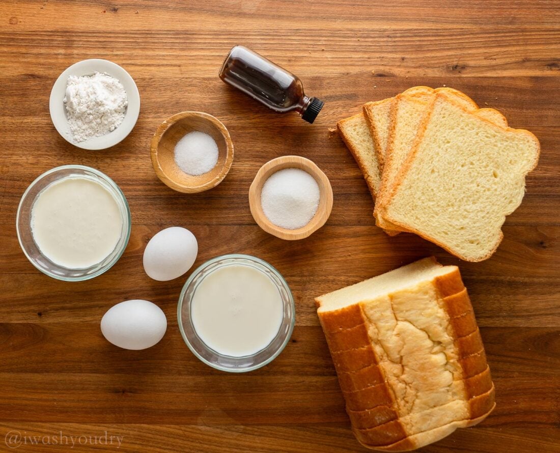 Ingredients for french toast sticks laid out on wood countertop. Bread, eggs, sugar, vanilla, milk, cream.