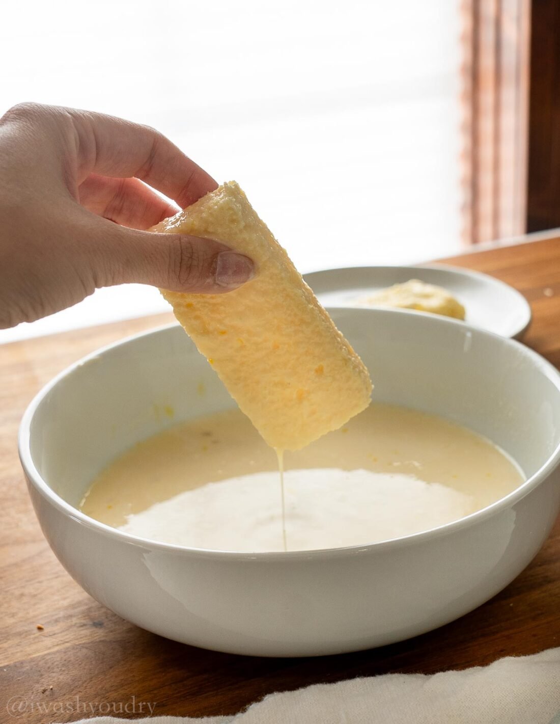 stick of bread being dunked into french toast batter