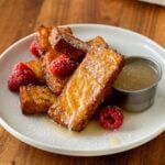 French Toast sticks stacked on a white plate with buttermilk syrup next to it