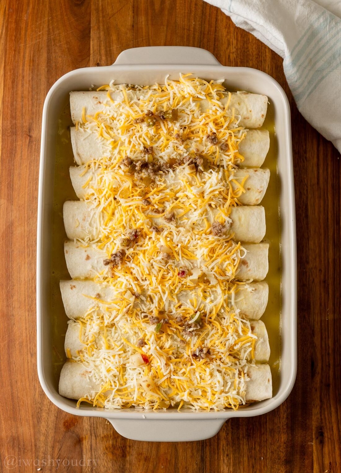 unbaked enchilada casserole with sausage and cheese on top.