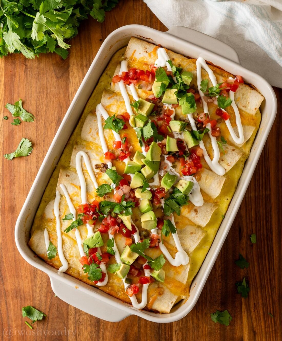 casserole dish with sausage egg and cheese enchiladas topped with avocado and tomatoes.