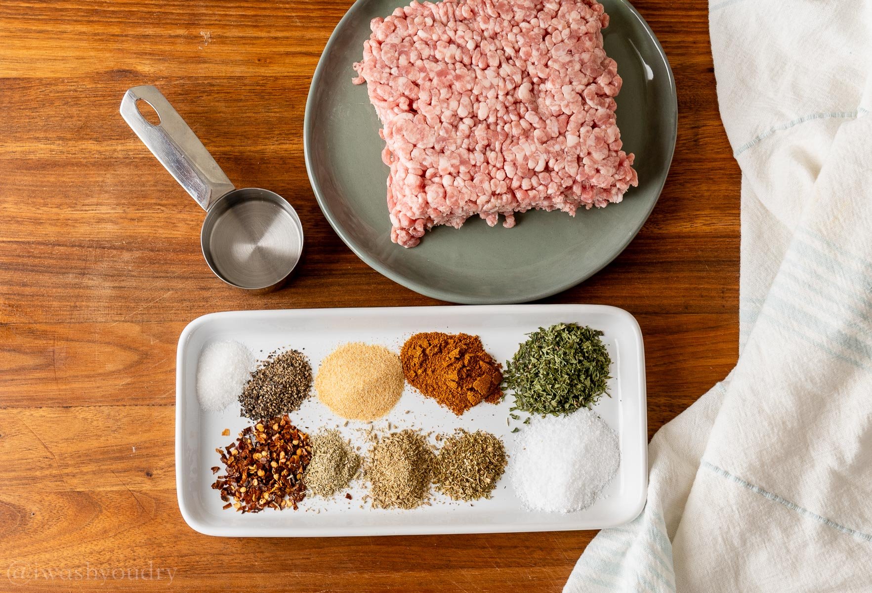 spices and herbs on a white tray with a plate of ground pork nearby.