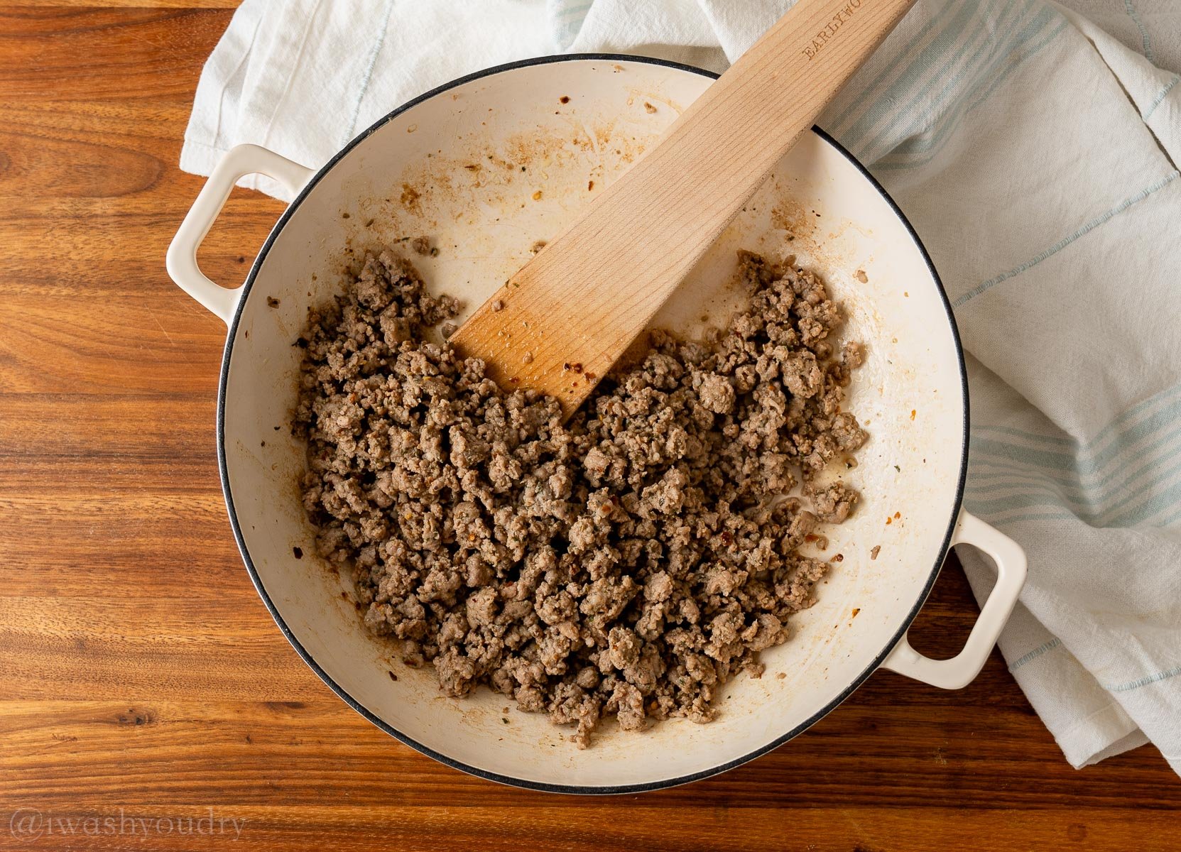 browned Italian sausage in white pan with wooden spoon inside.