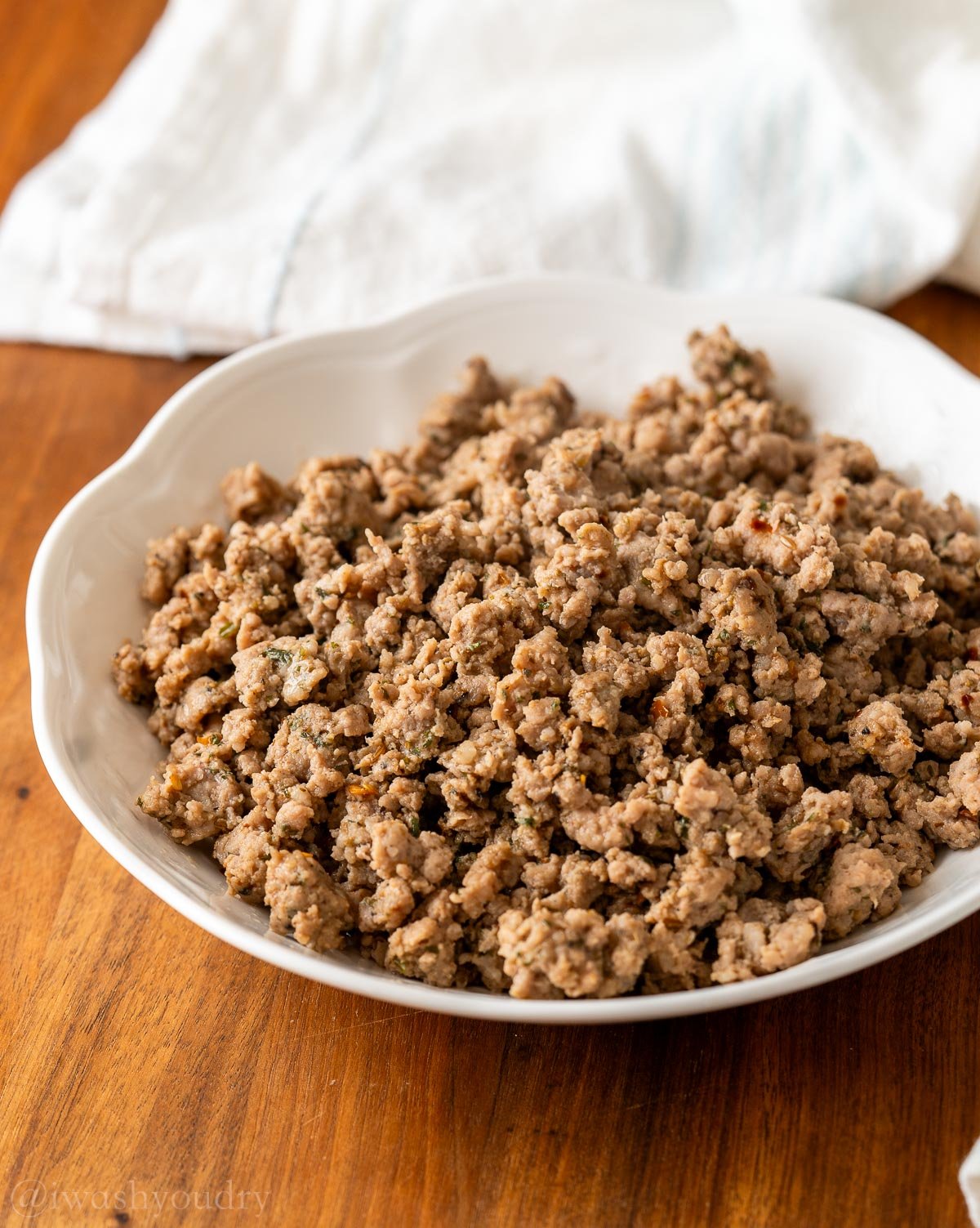 browned italian sausage in a white bowl on a wooden surface.
