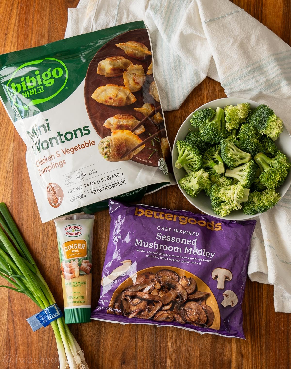 wontons and mushrooms in freezer bags on wooden surface with bowl of fresh broccoli nearby.