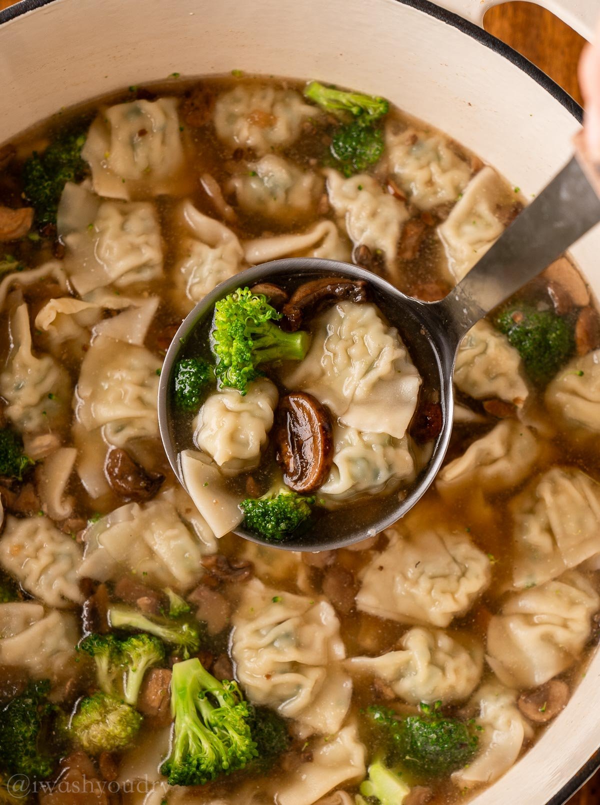ladle full of wonton soup with mushrooms and broccoli.