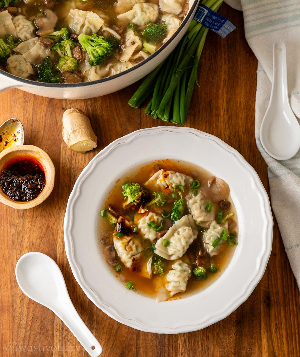 white bowl filled with wontons, mushrooms and broccoli in a chicken broth.