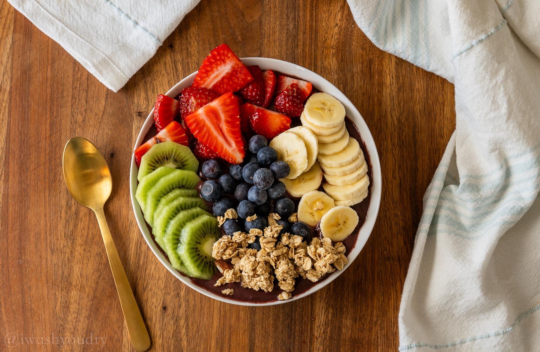 smoothie bowl with strawberries, blueberries, kiwi, bananas and granola with a spoon next to it.
