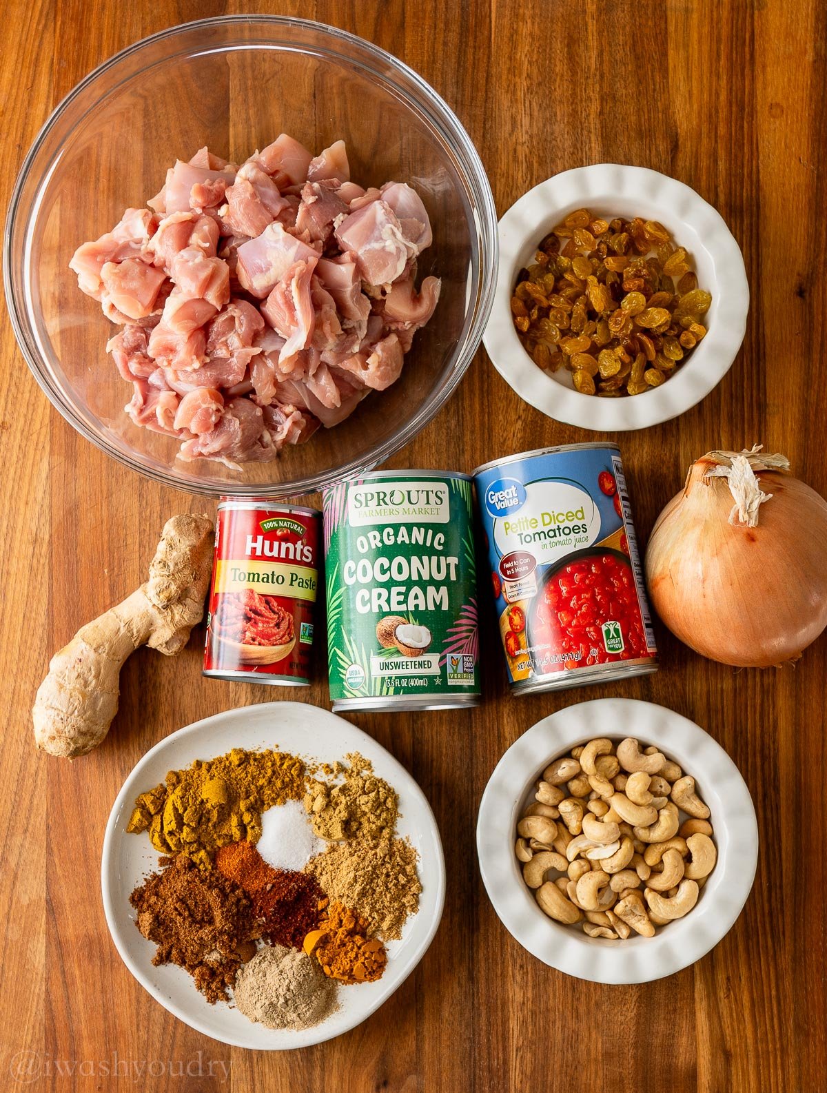 Ingredients for chicken coconut korma on a wooden surface with spices and ginger.