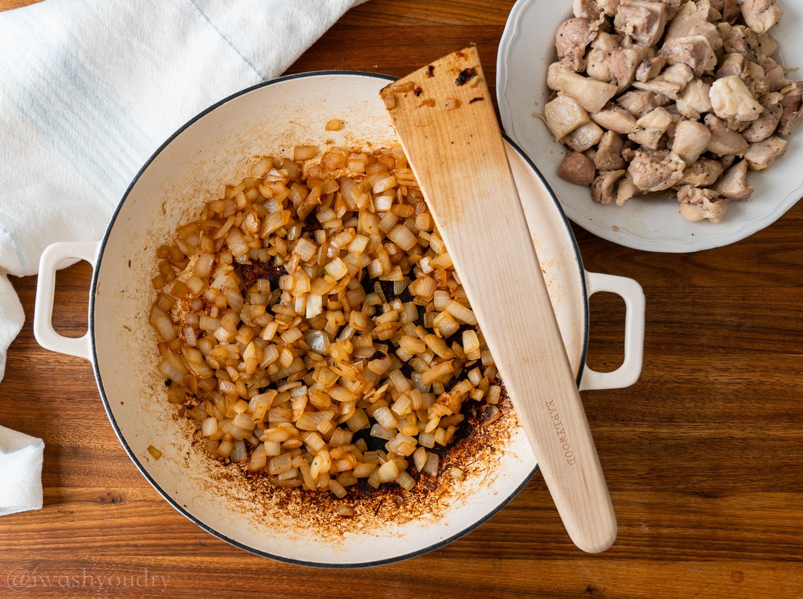 Caramelized onions in a pan with wooden spoon on top. Bowl of cooked chicken pieces nearby.