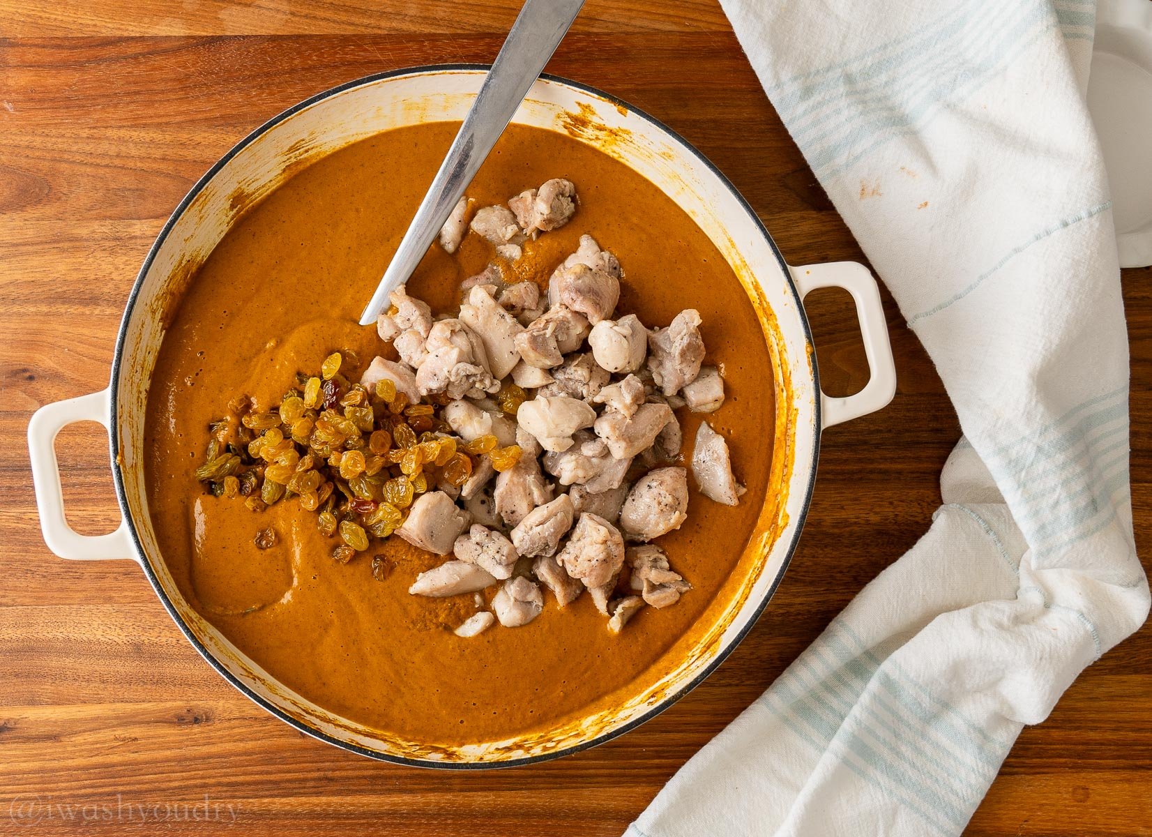 chicken and raisins in blended curry sauce in saucepan.
