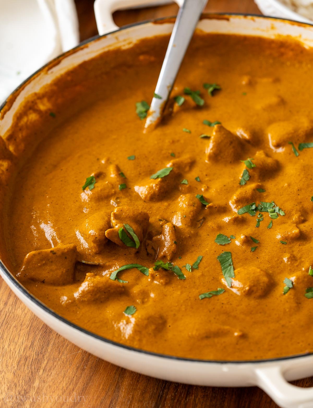 pan with curry and chicken in it as well as a silver spoon. Dish is topped with a light sprinkle of cilantro.