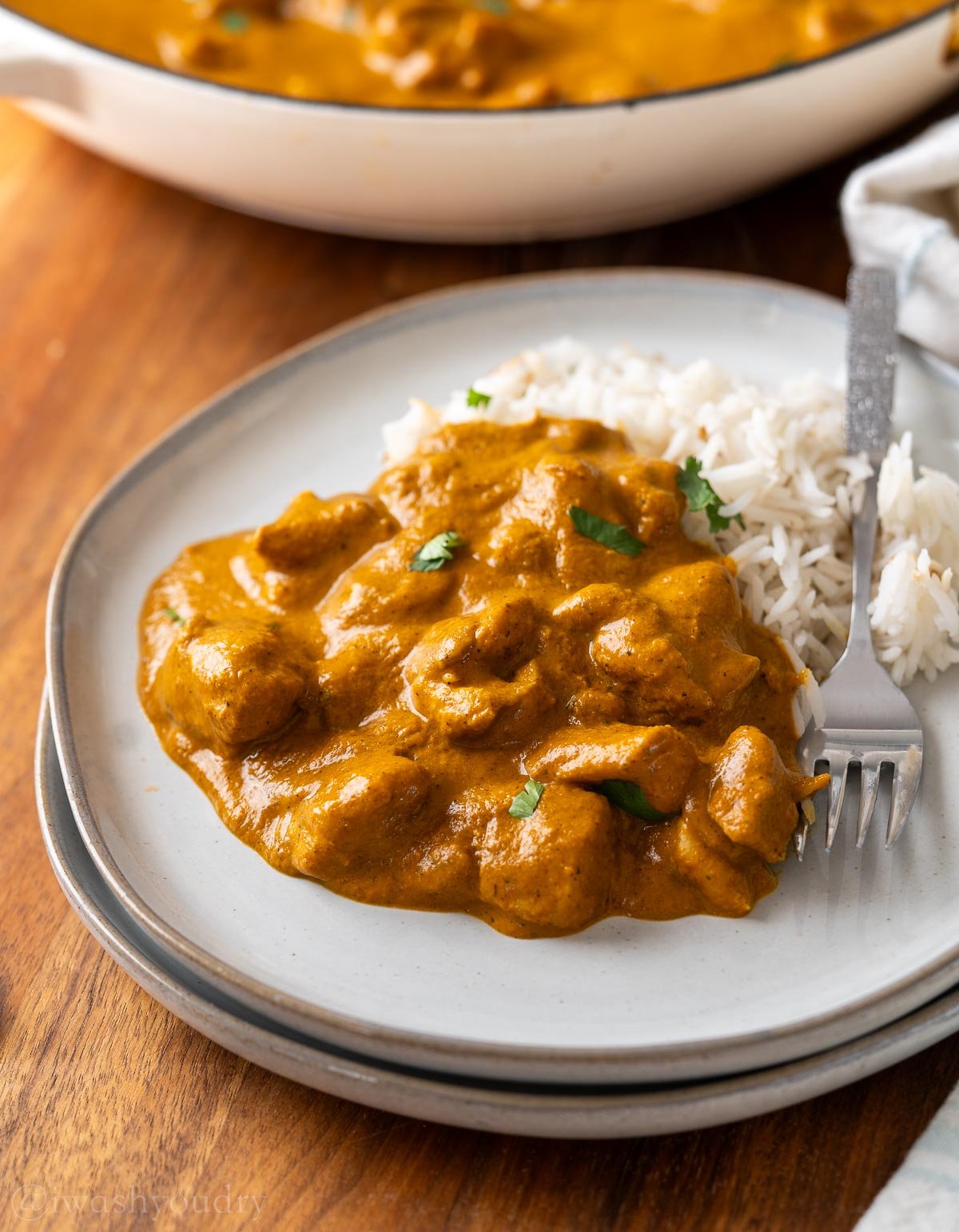 plate with creamy coconut chicken korma served with a side of white rice.