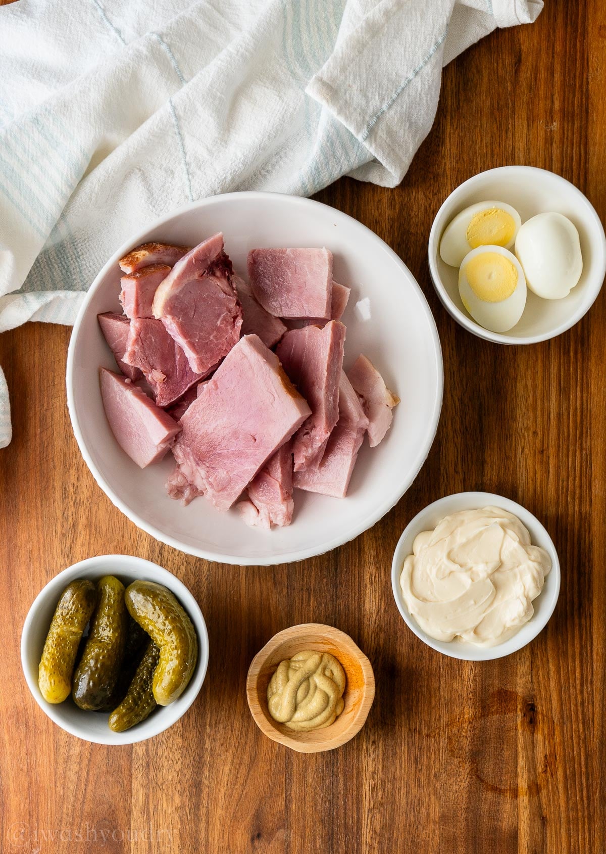 ingredients for ham salad on a wooden surface with hard boiled eggs and pickles.