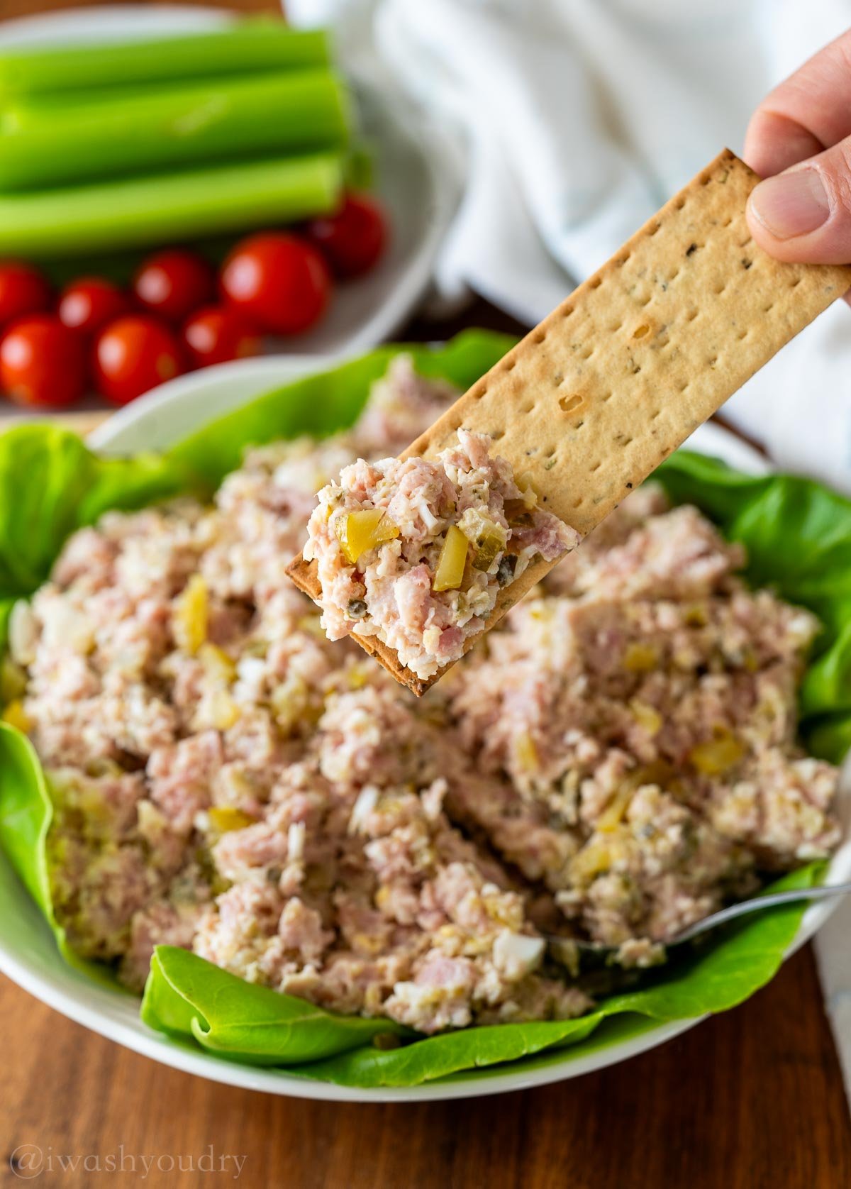 cracker full of ham salad with tomatoes and celery in the background.