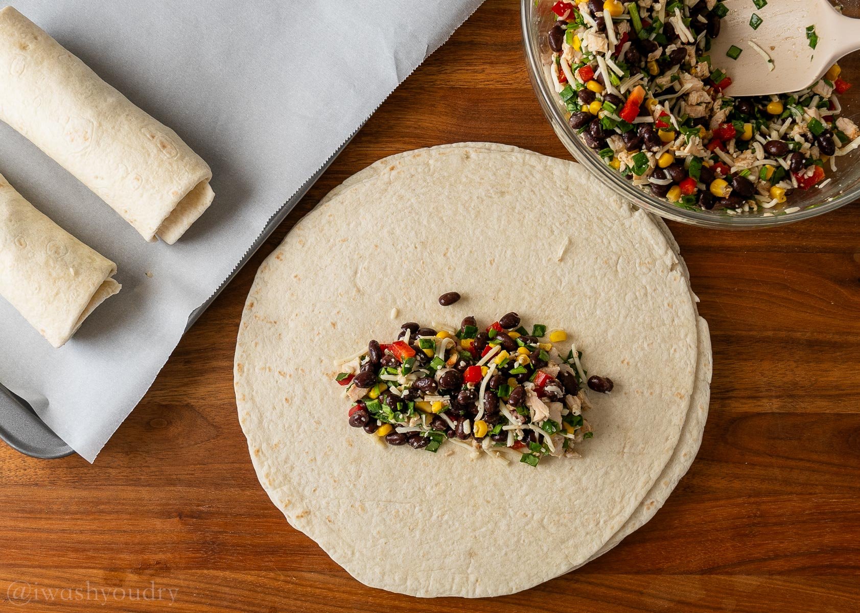 egg roll filling in the center of a tortilla with rolled up tortillas on a tray next to it.