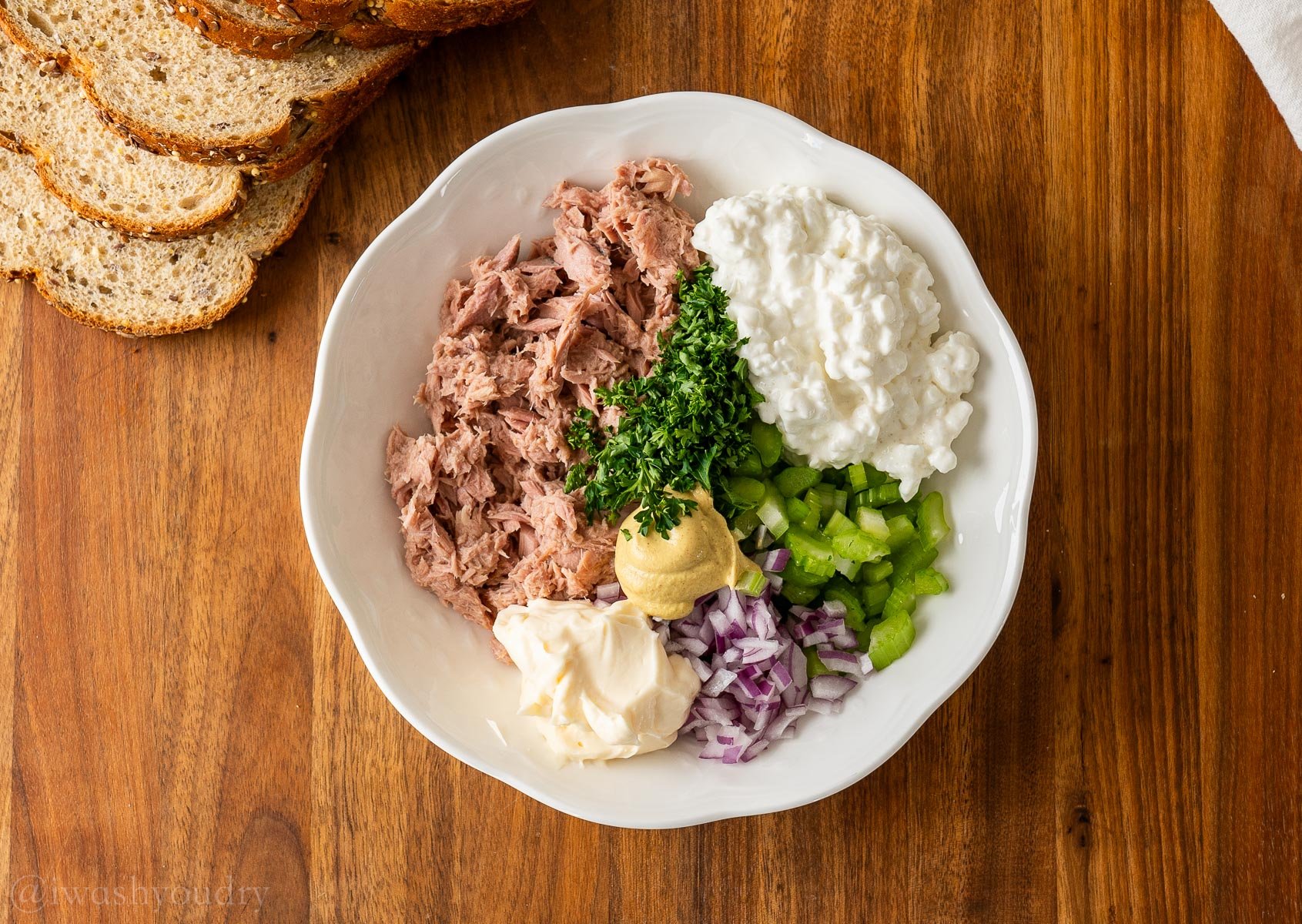 Ingredients for Tuna Salad in white bowl with slices of bread next to it.