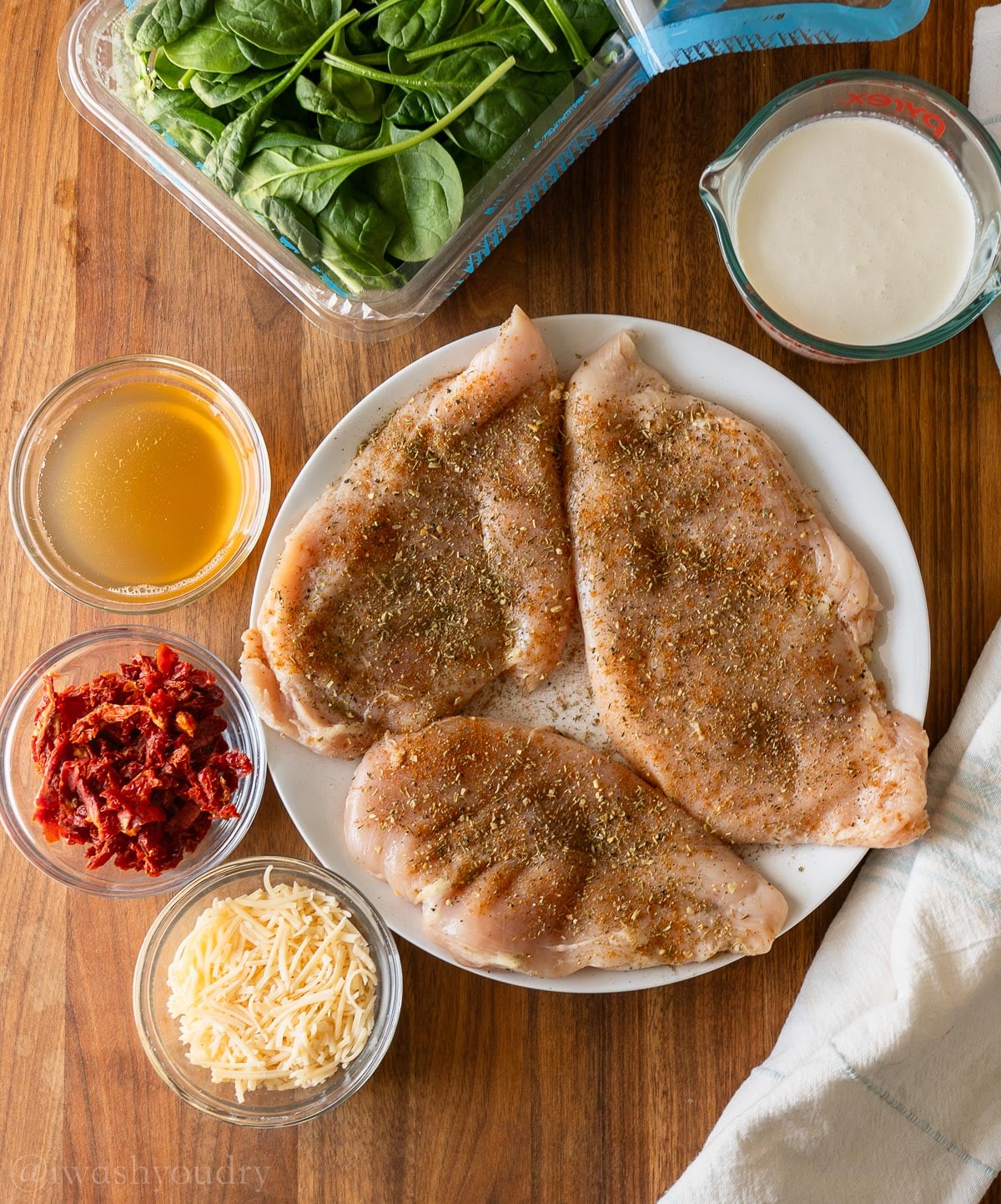 Ingredients for Tuscan Chicken on wooden surface with sun dried tomatoes, spinach and parmesan cheese.