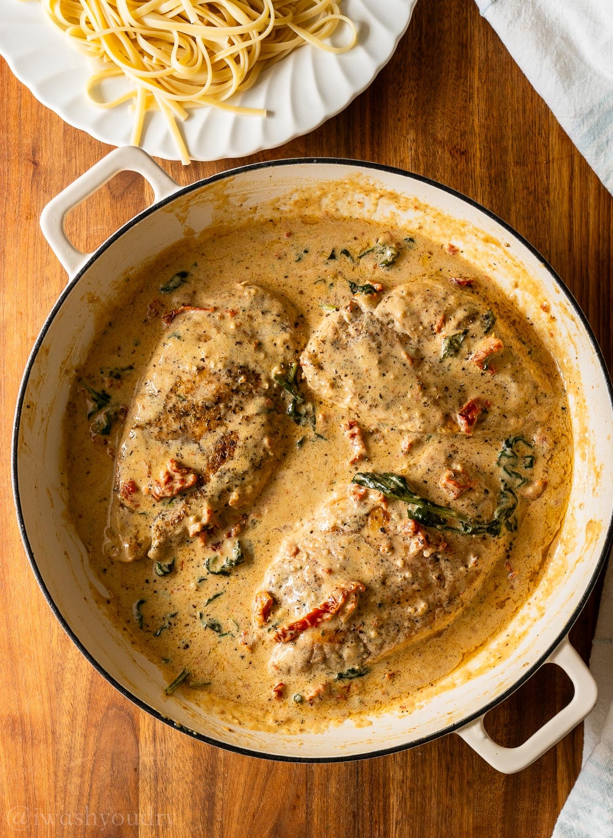 cooked creamy tuscan chicken recipe in white pan with orange sauce.