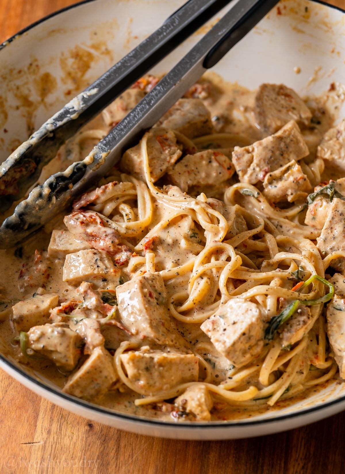 twirly noodles in tuscan chicken sauce with tongs.