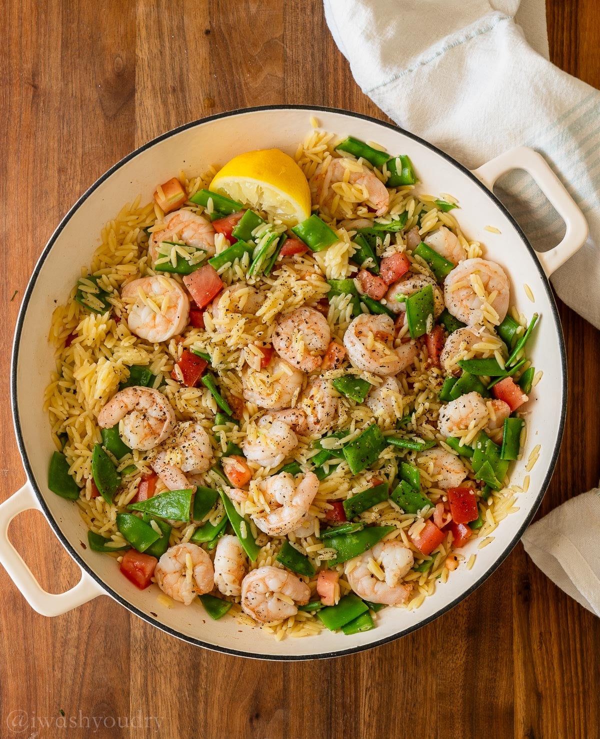 Lemon pepper shrimp in a skillet with orzo pasta, snow peas and tomatoes.
