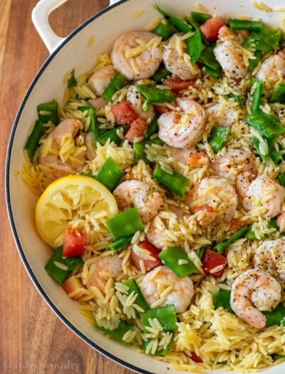 Lemon pepper shrimp orzo pasta in a skillet with a lemon wedge as well.