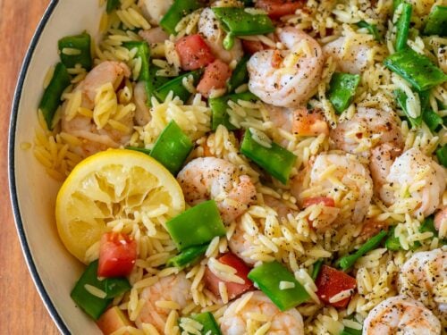 Lemon pepper shrimp orzo pasta in a skillet with a lemon wedge as well.
