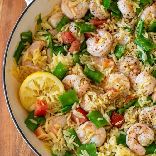 Lemon pepper shrimp orzo pasta in a skillet with a lemon wedge as well.