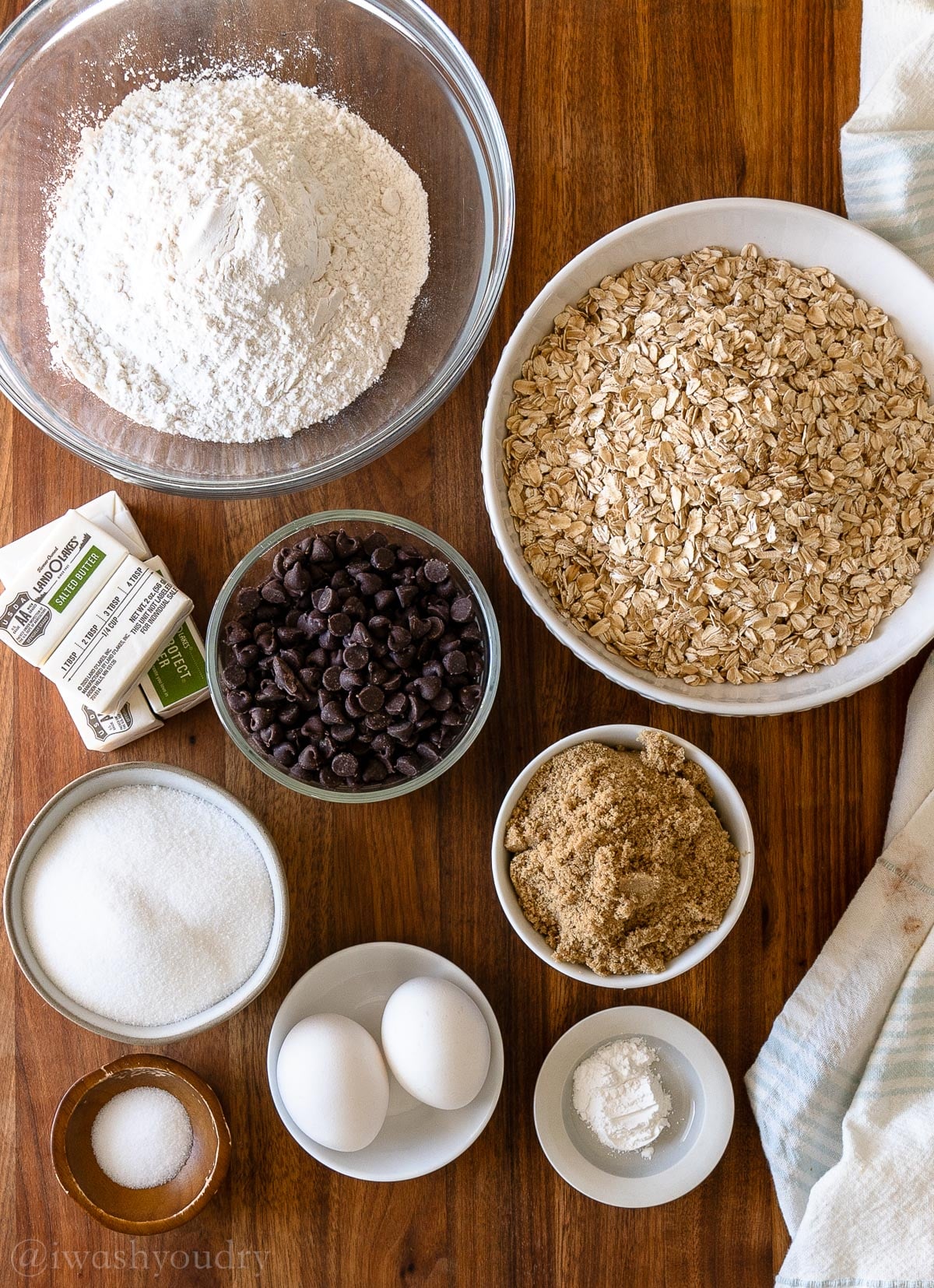 Ingredients for oatmeal chocolate chip cookies on a wooden surface with brown sugar and butter.