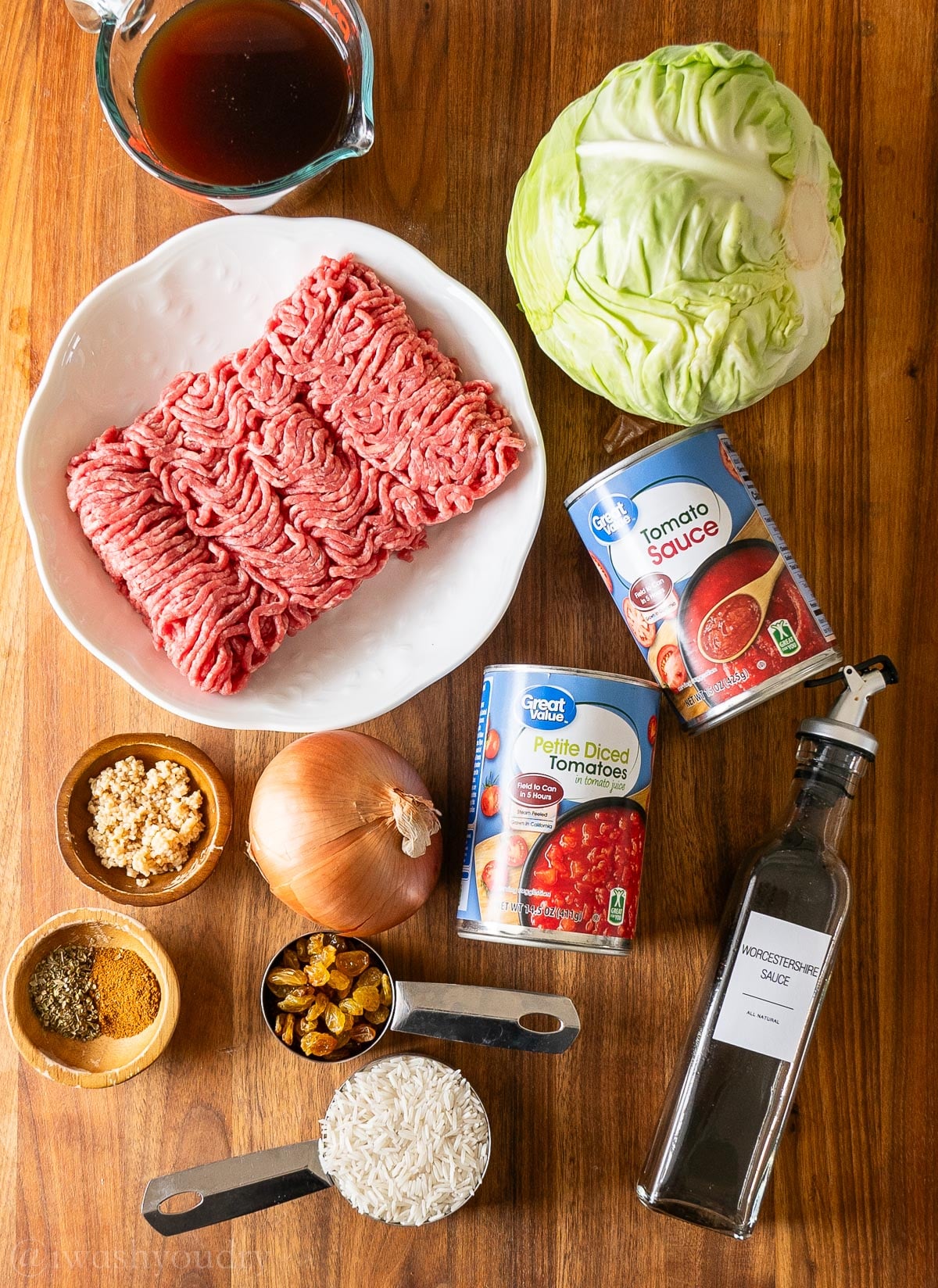 Ingredients for cabbage rolls on a wooden surface - including ground beef, cabbage, diced tomatoes and onion.