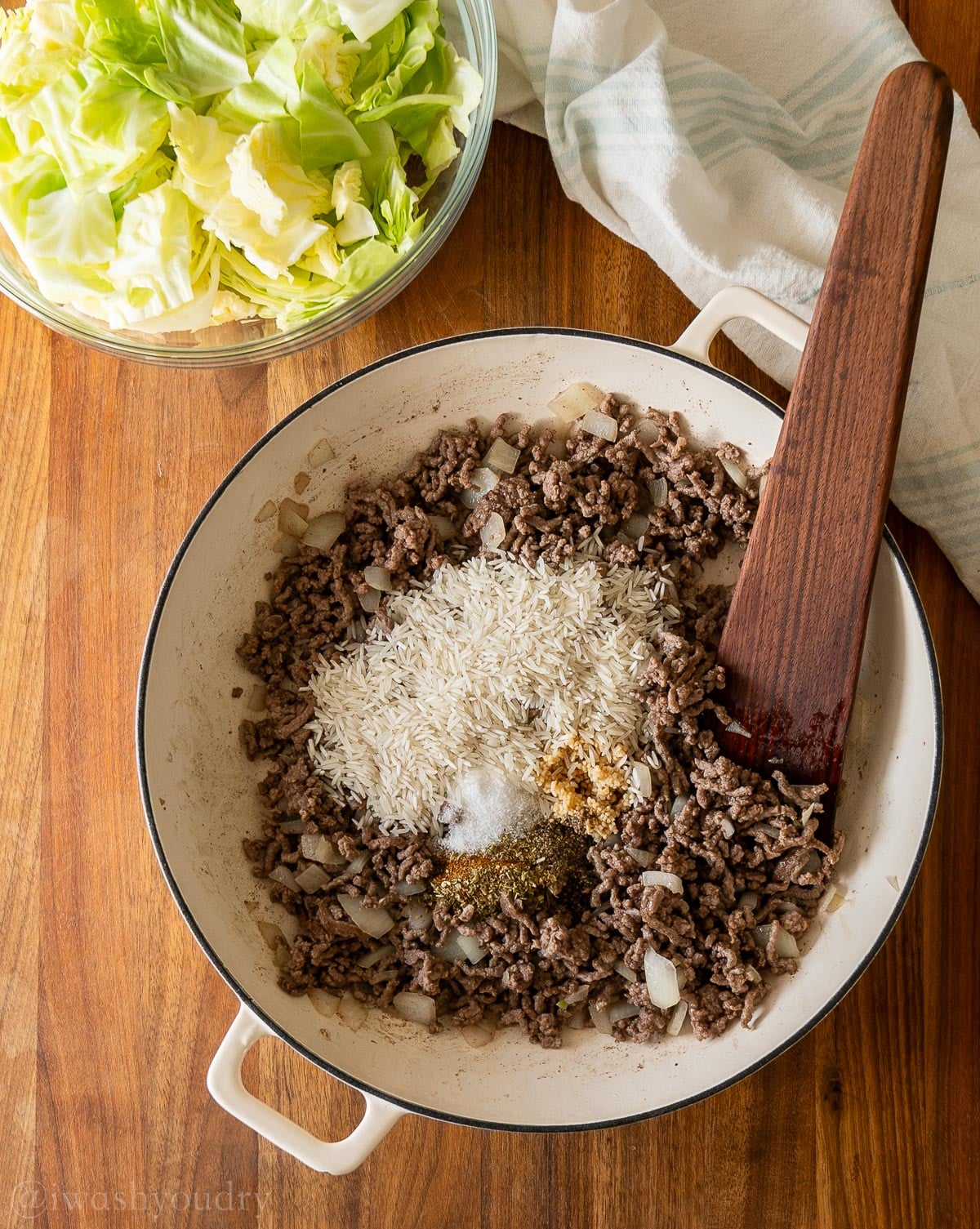 browned ground beef in skillet with uncooked rice and seasonings inside.