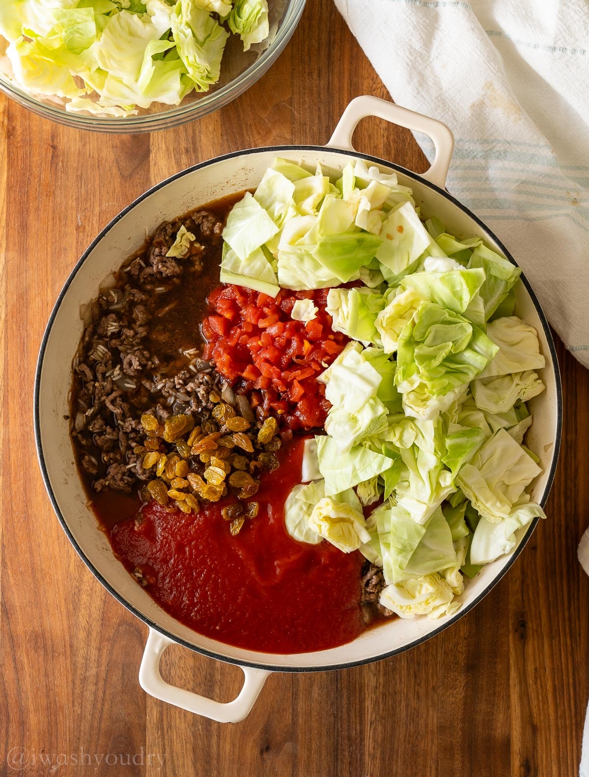 Ground beef with rice, cabbage, beef broth and diced tomatoes in skillet, topped with golden raisins.