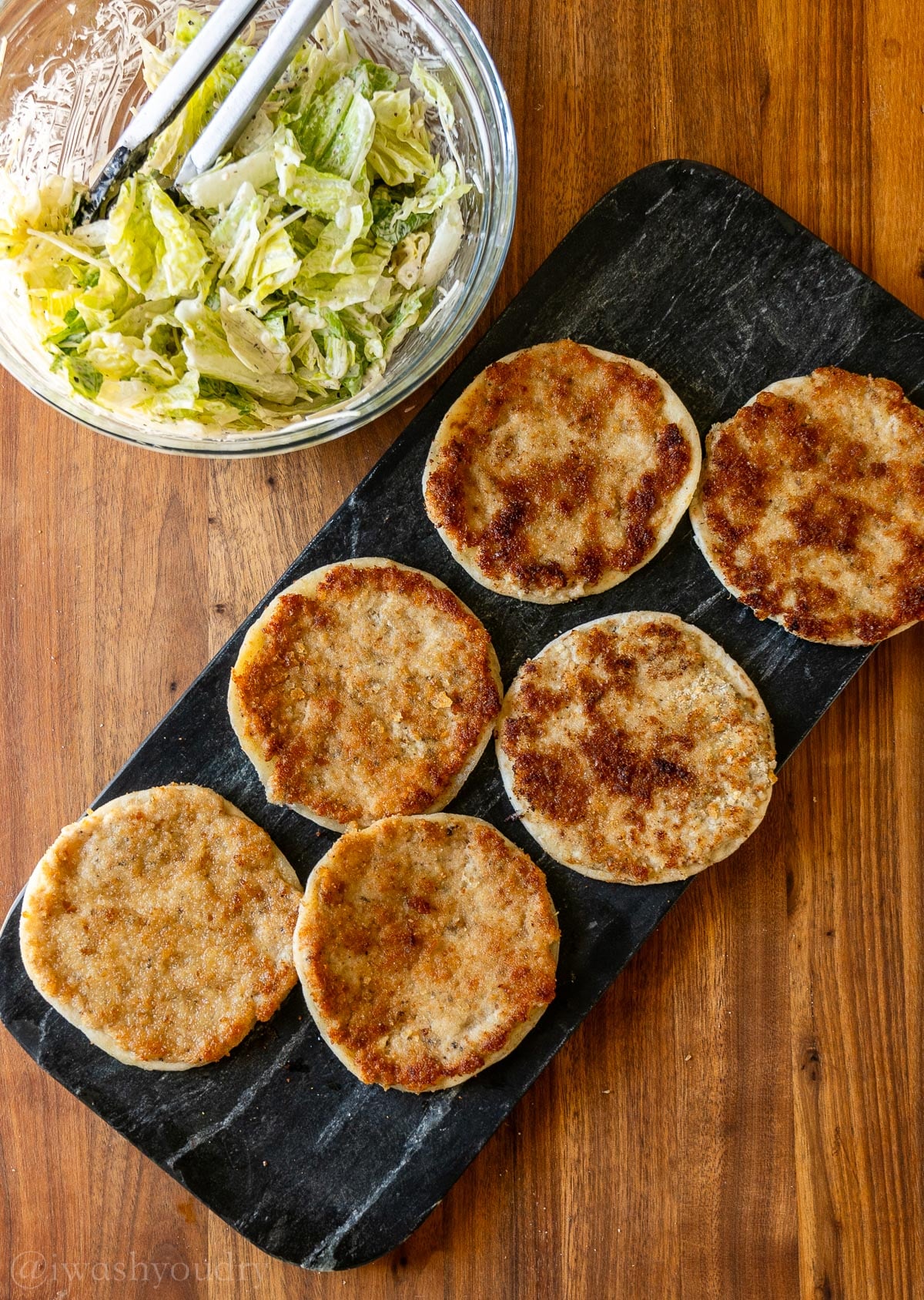 Crispy chicken on tortillas with a bowl of Caesar salad next to it.