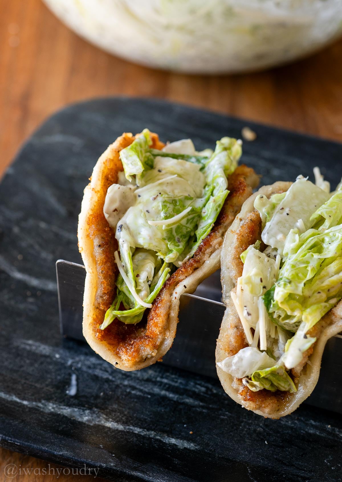 Crispy Chicken Caesar Smash Taco in taco tray on black plate.