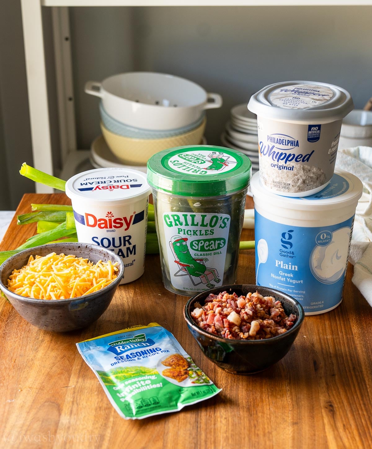 ingredients for grillo pickle dip on wooden surface with cheddar cheese and bacon.