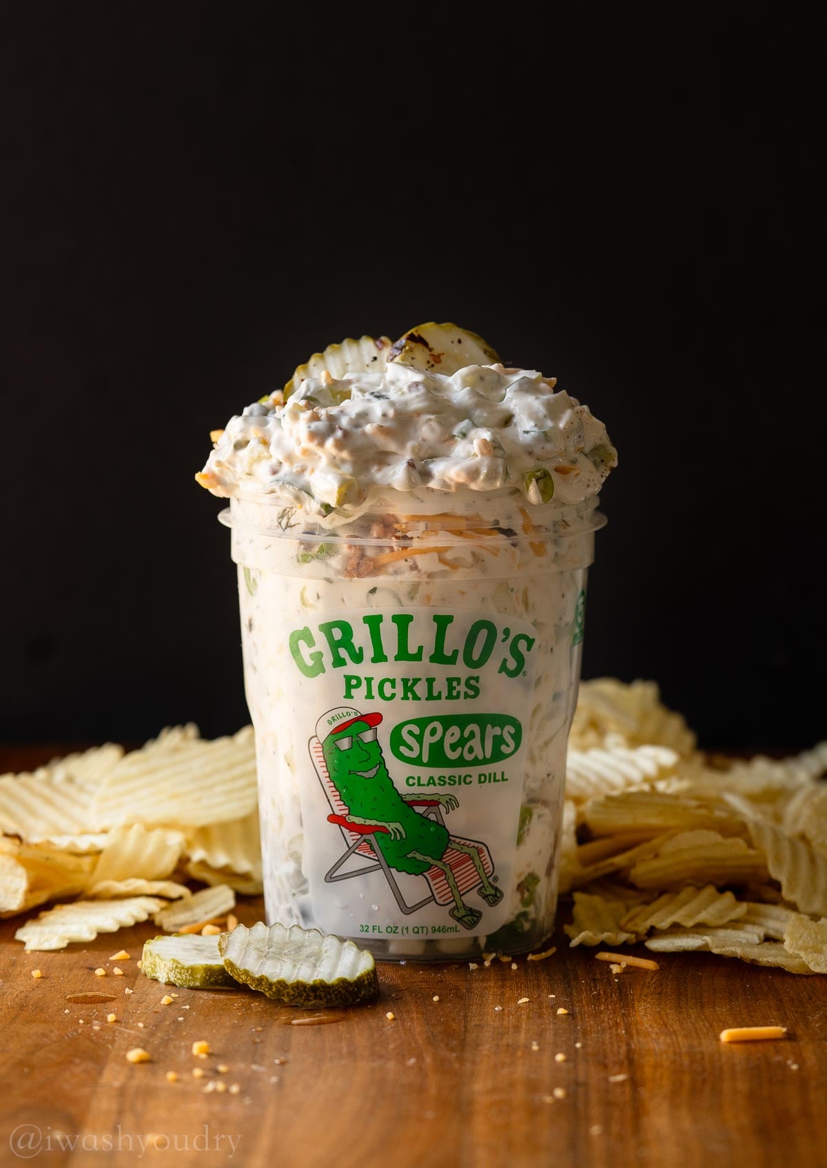 creamy dill pickle dip in grillos pickle tub with potato chips around it.
